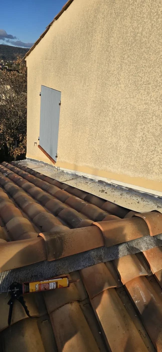 Solin en zinc posé contre un mur enduit, tuiles canal en pied