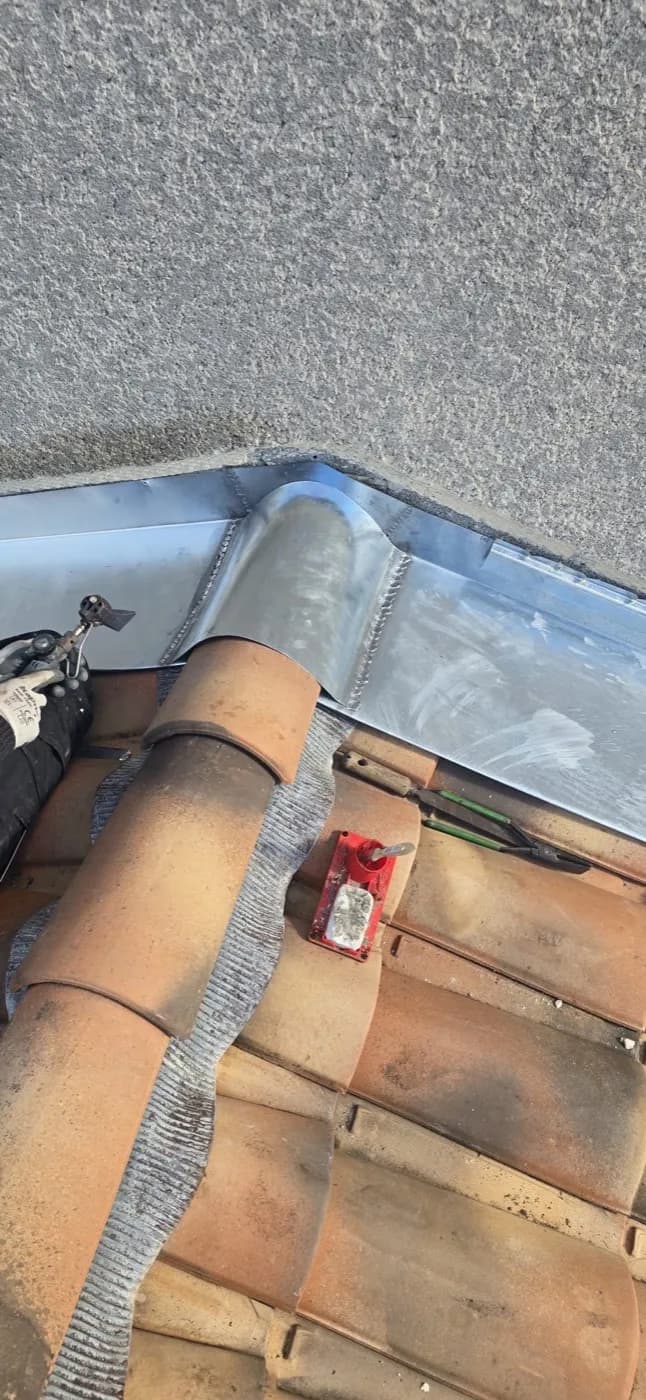 Angle d'un solin en zinc, avec ses soudures, contre un mur enduit