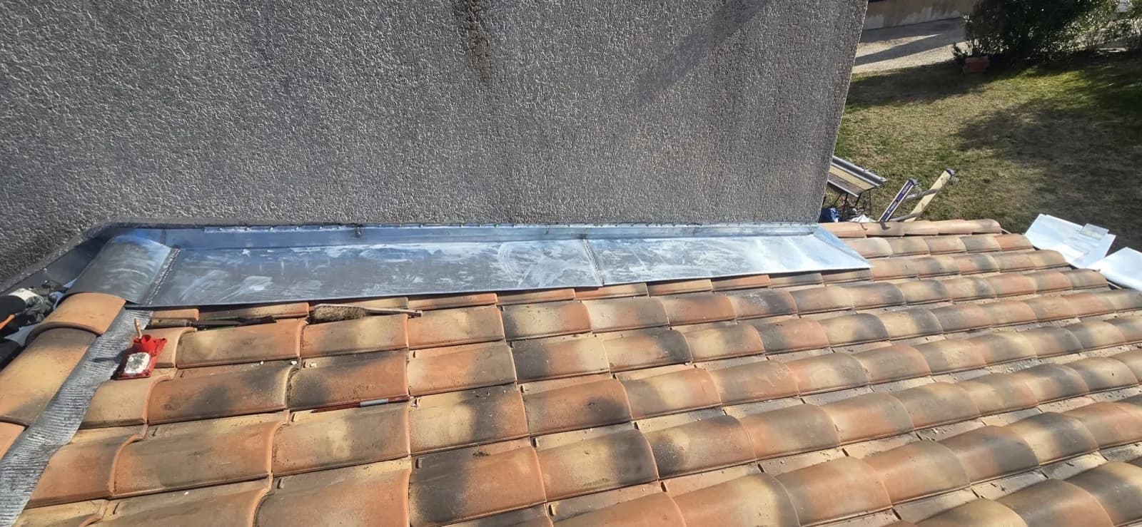 Solin en zinc entre une toiture en tuiles et un mur enduit